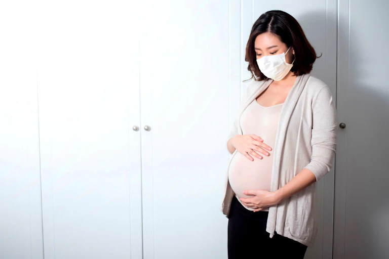 A pregnant woman wearing a face mask holds her stomach.