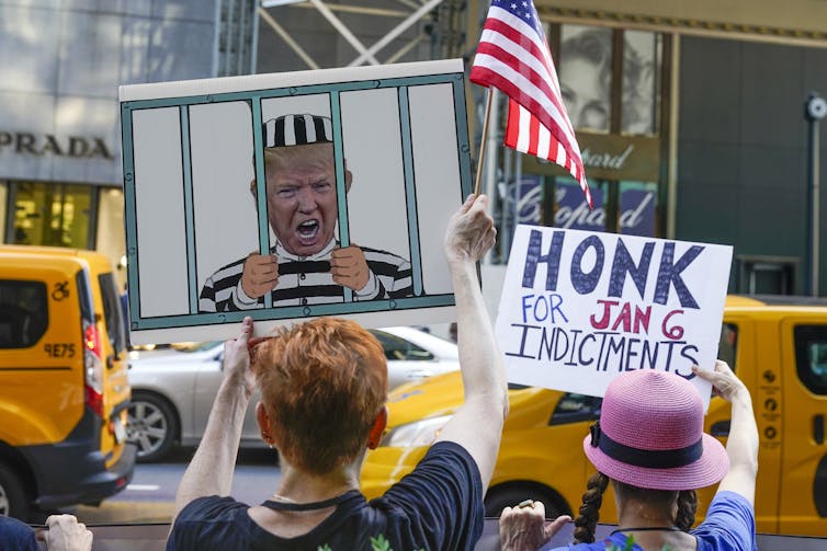 A protester holds up a sign with a caricature of Donald Trump behind bars.