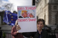 A woman holds up a sign depicting two men kissing.