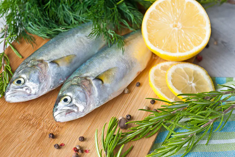 dos pescados, rodajas de limón y manojos de perejil sobre una tabla.