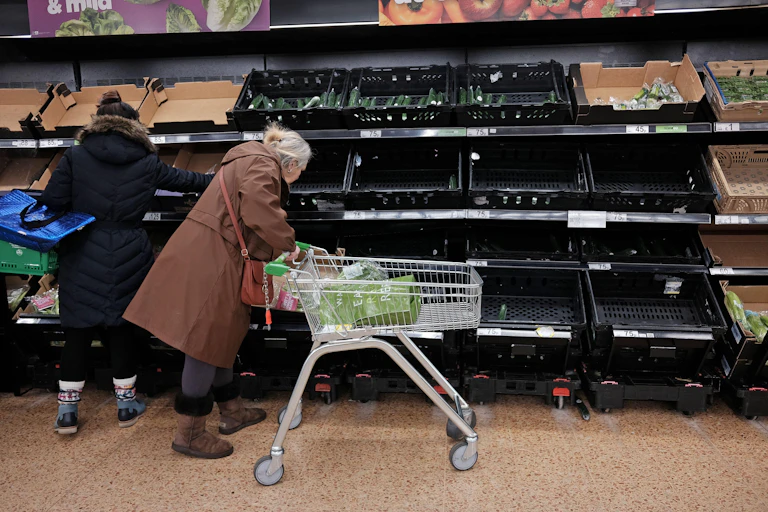 Two women standing in front of empty supermarket shelves.