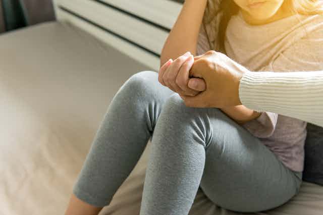 una chica sentada en el suelo con mallas grises extiende su mano, que es agarrada por alguien en señal de ayuda.