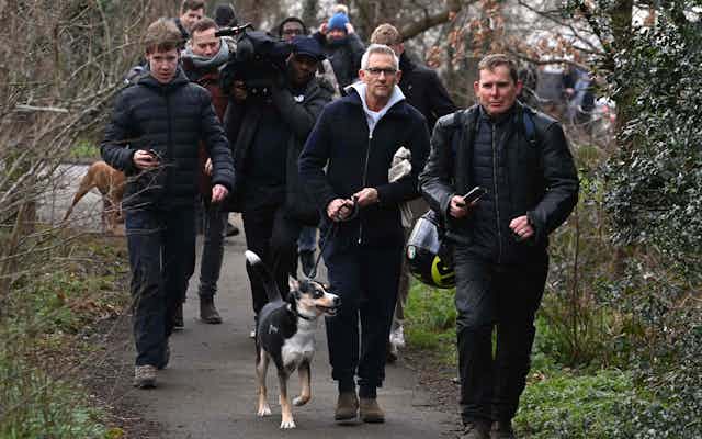 Gary LIneker and his dog out walking, surrounded by reporters