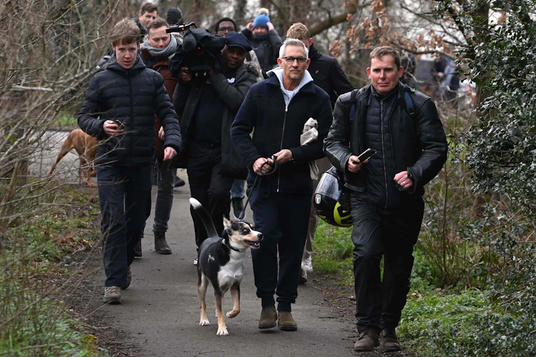 Gary LIneker and his dog out walking, surrounded by reporters