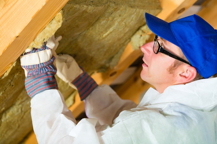 A man fitting insulating foam between wooden buttresses in a roof.