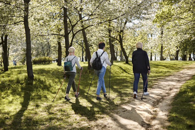 Three people, two with gray hair, walk with poles on a trail in springtime.