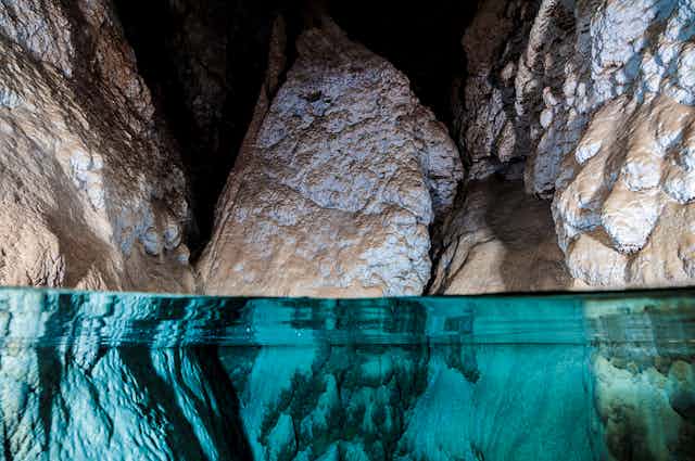 A close-up image of water in a cave, with three large rocks protruding out of clear water