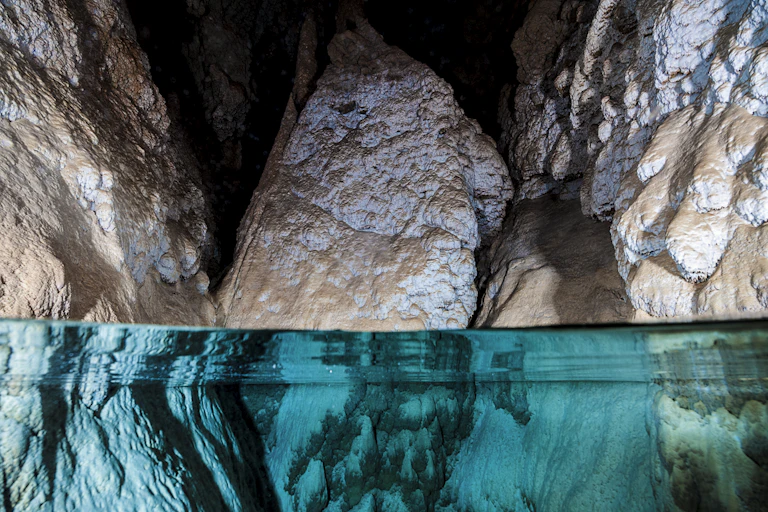 A close-up image of water in a cave, with three large rocks protruding out of clear water