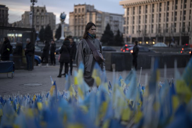 A woman stands outside looking at blue and yellow flags.