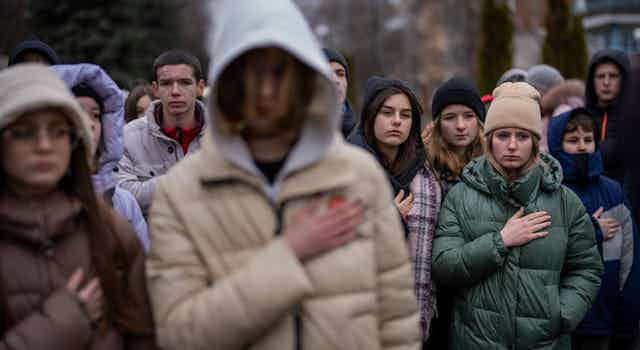 People seen standing with hands on their hearts.