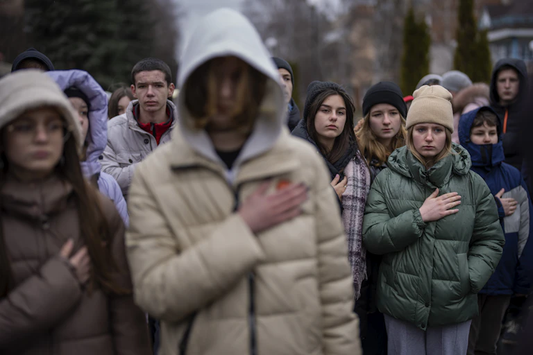 People seen standing with hands on their hearts.
