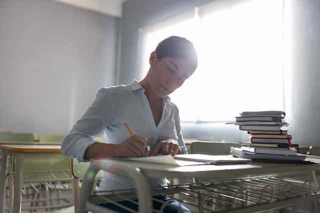 A person sits at a desk with papers and books stacked nearby.