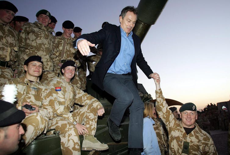 Tony Blair jumping from a tank in front of soldiers.