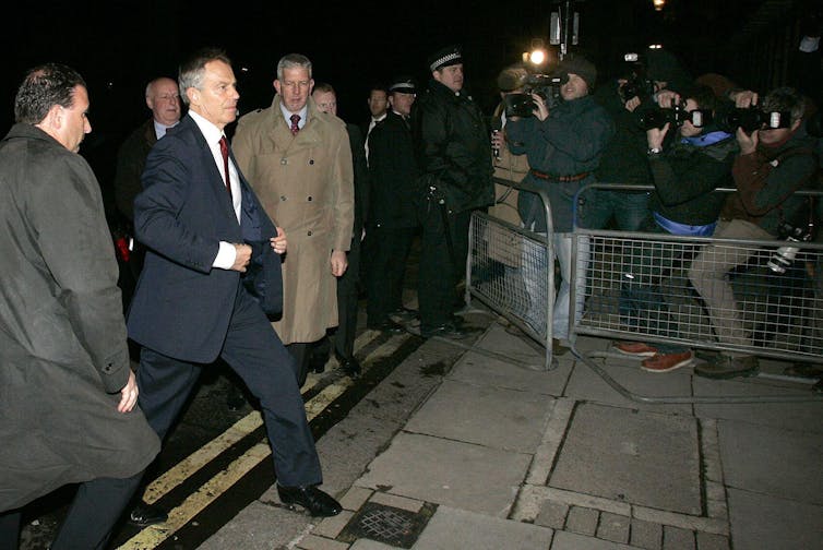 Tony Blair flanked by security guards, walking past the press.