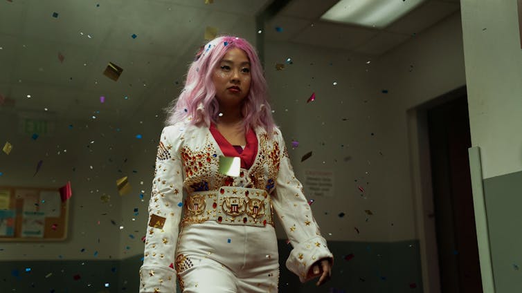 Stephanie Hsu has pink hair and wears an Elvis style white jumpsuit.