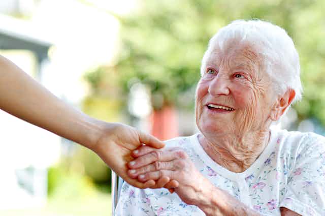 Une femme âgée tient en souriant la main d'une aide soignante