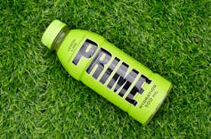 A green bottle with the word Prime in large black letters, lying on grass.