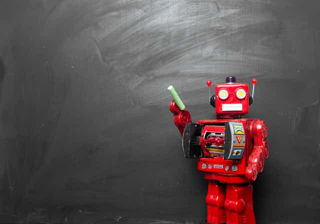 A toy robot holding a piece of chalk stands in front of a blank chalkboard
