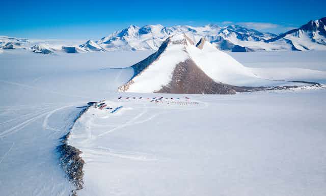 A "nunatak" or glacial island protrudes high above the polar ice cap, dwarfing the Princess Elisabeth Station in Dronning Maud Land.
