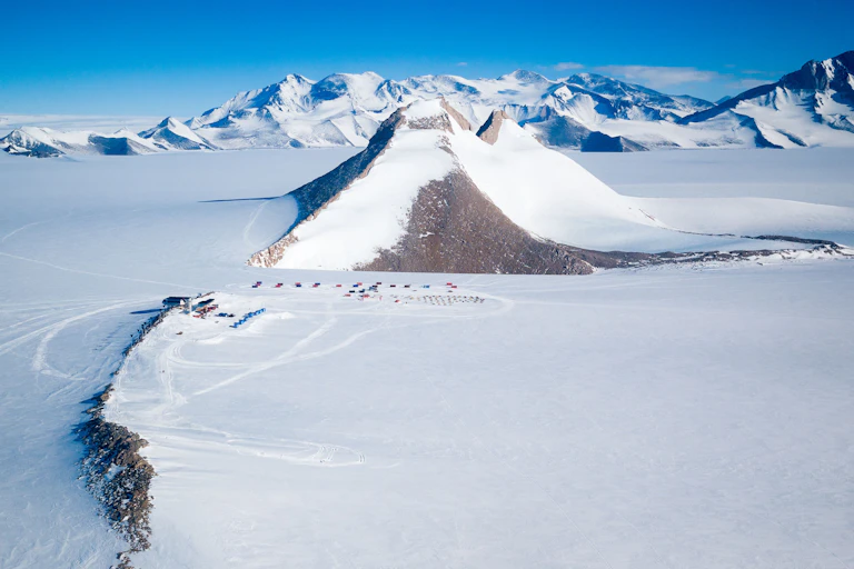 A "nunatak" or glacial island protrudes high above the polar ice cap, dwarfing the Princess Elisabeth Station in Dronning Maud Land.