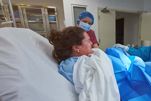 una mujer dando a luz con una matrona al lado de la cama.