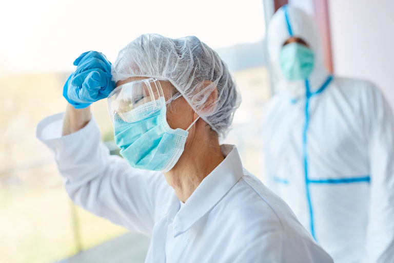 Una sanitaria abatida vestida con EPI es observada por un sanitario vestido con EPI.