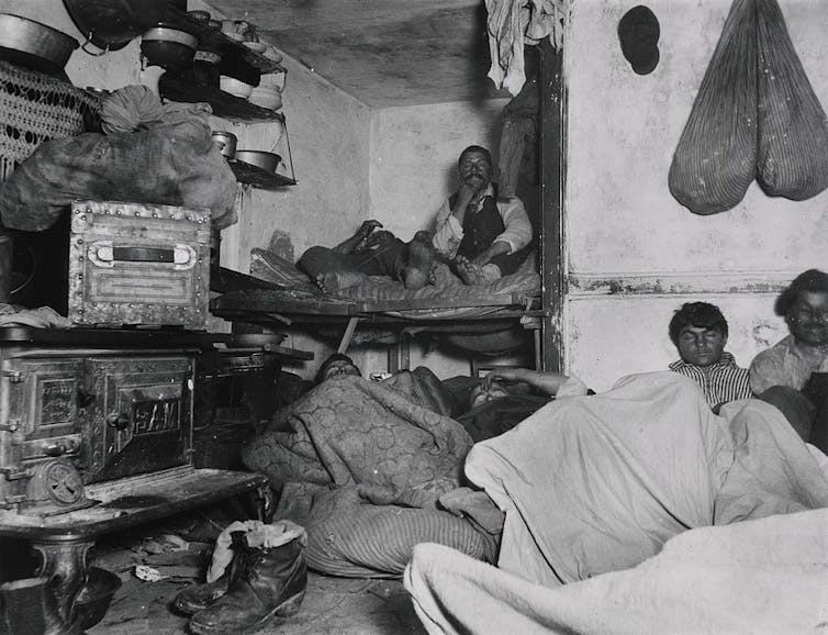 Muchos hombres durmiendo en literas y colchones en una pequeña habitación.