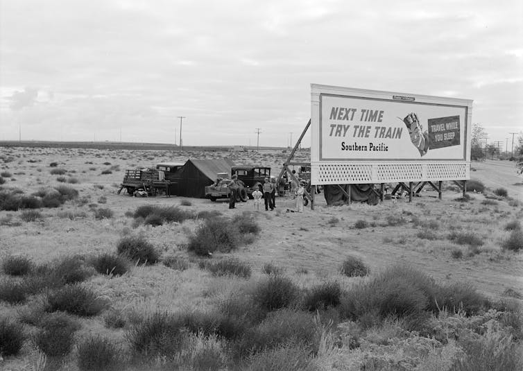Three families camped behind an advertising billboard that serves as a windbreak.
