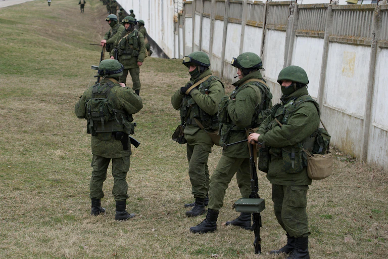 Men in green uniforms in front of a wall.