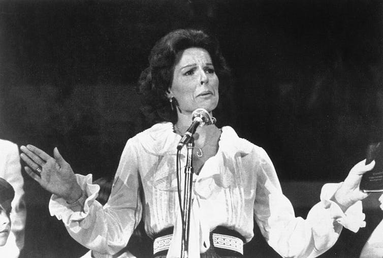 Black and white photo of woman speaking at a microphone.