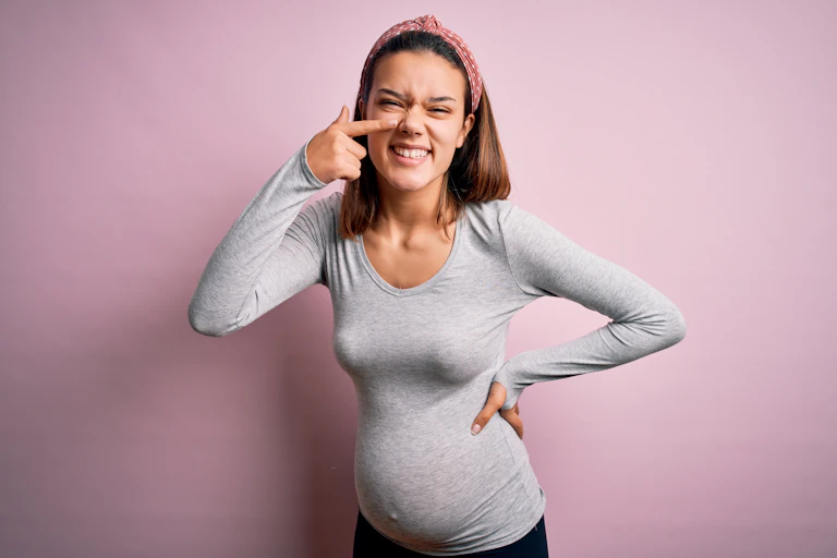 Une femme enceinte montre son nez en souriant/grimaçant.