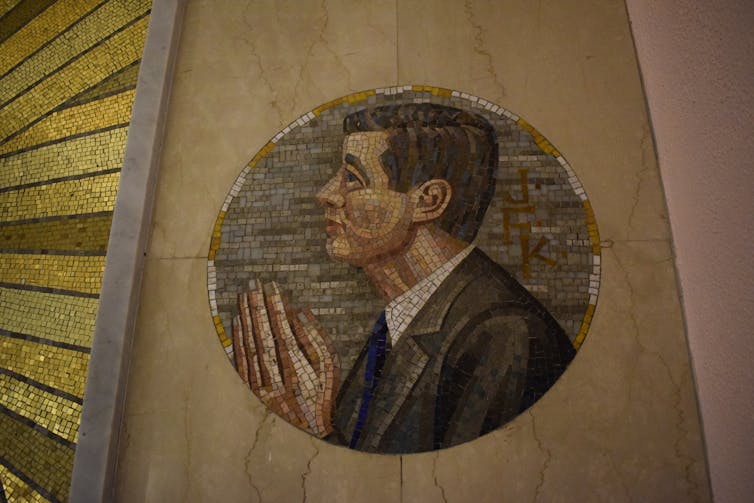 A mosaic shows a man wearing a suit holding his hands in a prayer position.