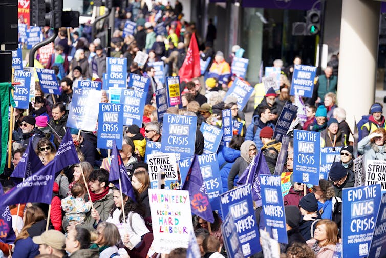Group of protesters with signs saying'End the NHS crisis' and'We support NHS workers'.