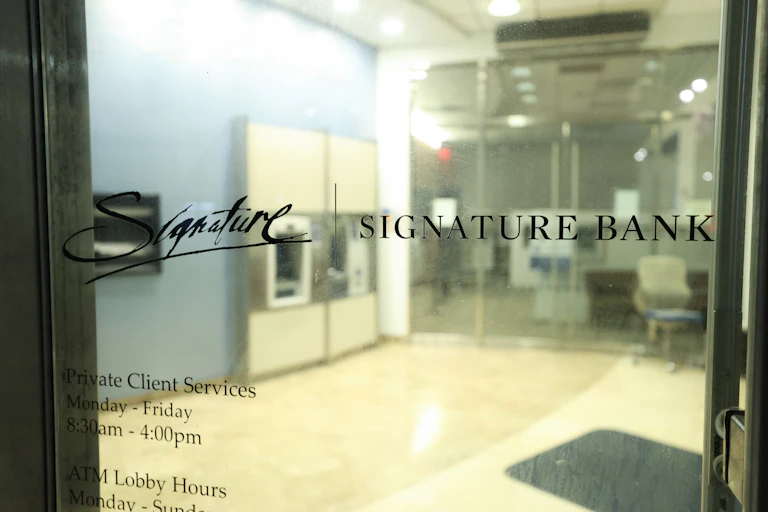 Closed glass doors show the Signature Bank logo. ATM machines and the bank's lobby appear in the background.