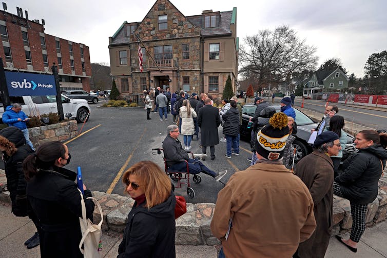 Dressed in winter clothing, people line up outside to enter their local bank.