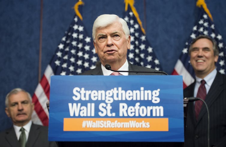 A man stands in front of a row of American flags and behind a lectern draped by a sign that says Strengthening Wall Street Reform