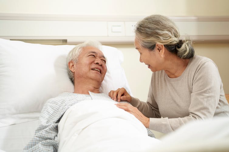 A woman with gray hair sitting beside a man with gray hair in a bed