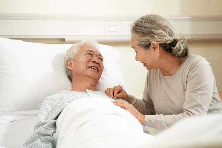 A woman with gray hair sitting beside a man with gray hair in a bed
