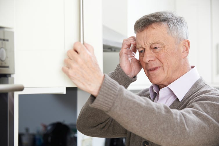 A older man looking into a kitchen cupboard and scratching his head