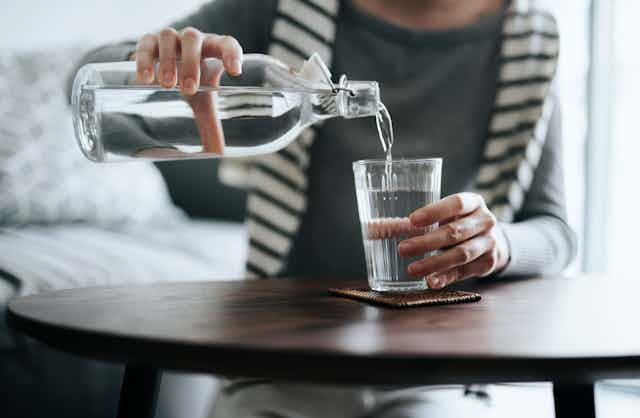A woman pouring water from a bottle into a cup.