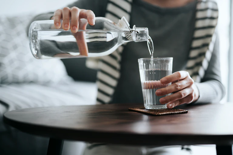 A woman pouring water from a bottle into a cup.