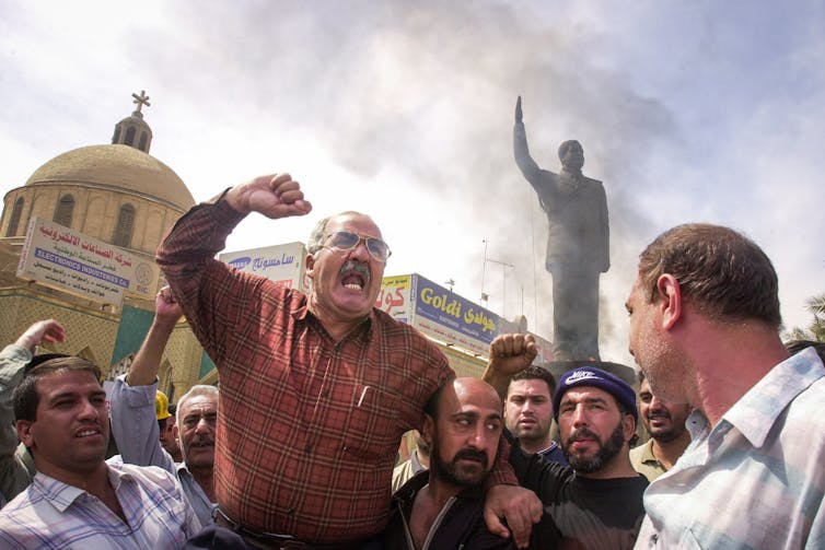 Iraqis cheer statue of Saddam Hussein on fire.
