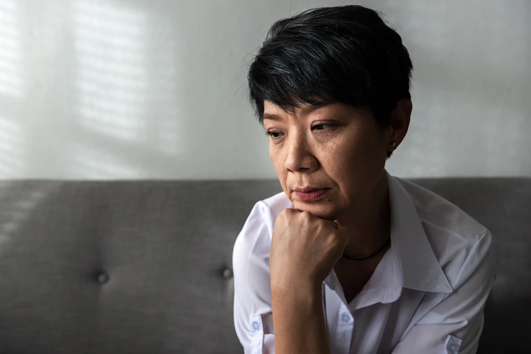 A woman sit with her hand on her chin, with a sad expression.