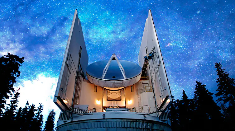 A radio dish antenna pointing at a dark blue sky, shown from a low angle