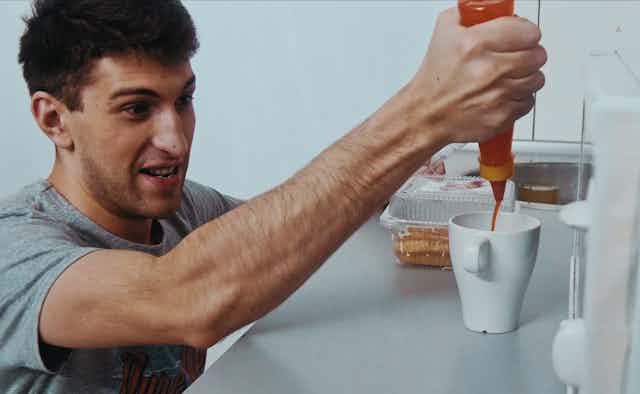 Young man in the kitchen putting hot sauce in a mug