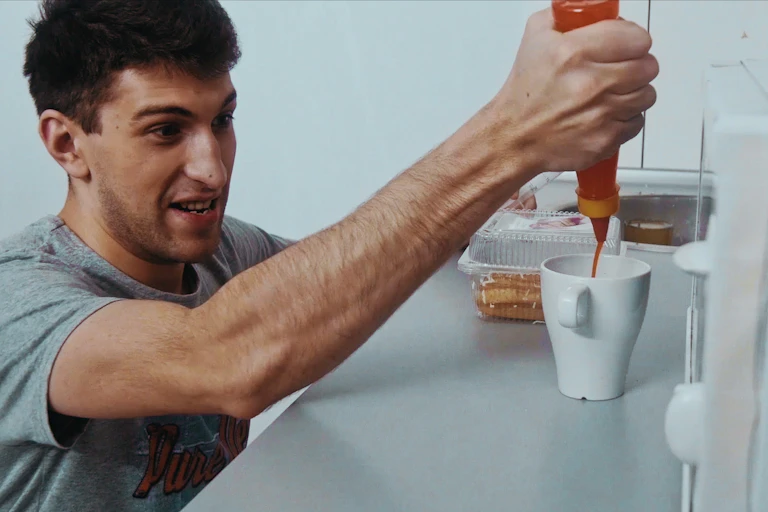 Young man in the kitchen putting hot sauce in a mug