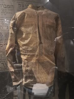 An SS uniform made out of Torah scroll, in a glass case on display at a museum.