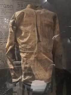 An SS uniform made out of Torah scroll, in a glass case on display at a museum.