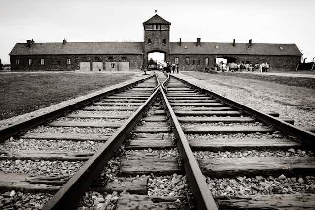 Black and white photo of buildings at Auschwitz death camp, with railway tracks in the foreground