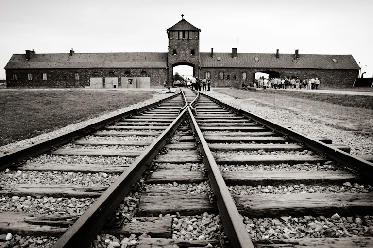 Black and white photo of buildings at Auschwitz death camp, with railway tracks in the foreground